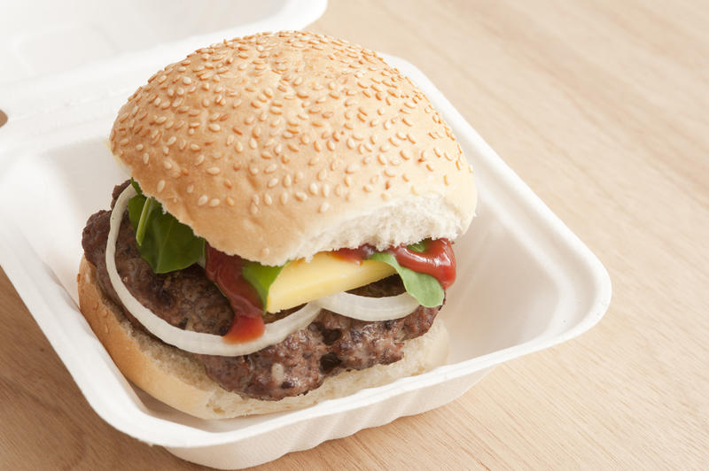 Hamburger takeaway in a disposable container with a thick juicy beef patty, salad trimmings and a slice of cheese