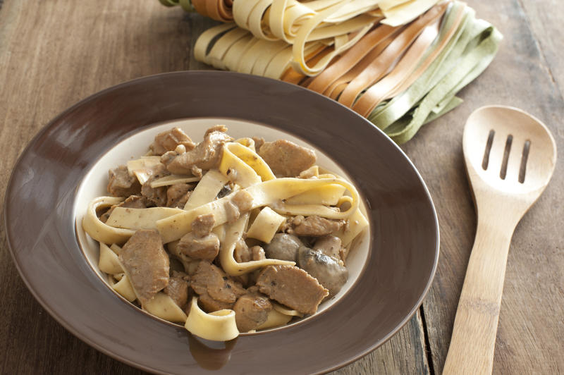 Tasty noodle and meat dish besides slotted spoon and dry ribbons of colorful pasta