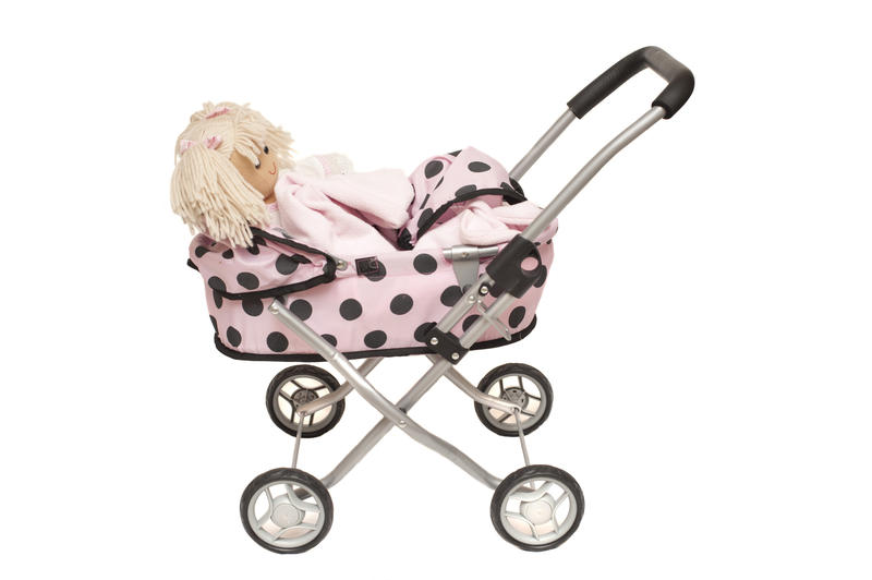 Blond doll in a kids toy pram with a feminine pink polka dot pattern isolated on white, side view