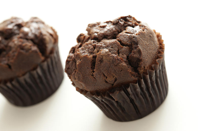 Two homemade delicious chocolate chip muffins with brown cupcake wrapper, oblique close up with copy space