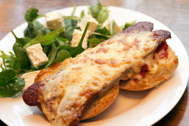 Spicy chorizo sausage with melted cheese served on a bun with feta and baby spinach salad on the side