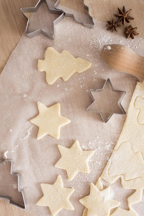 Baking traditional Christmas and seasonal biscuits with an overhead view on cutout raw pastry in star and tree shapes with dough and cookie cutters on a wooden kitchen table