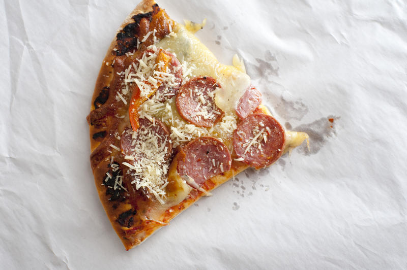 Triangular slice of pepperoni pizza with peppers and extra parmesan cheese as seen from an overhead view