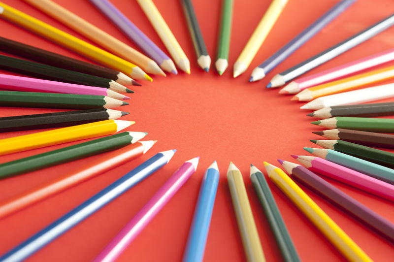 Various colored pencil tips facing each other and forming a ring over deep red background