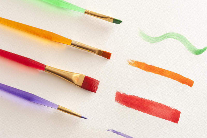 Four paintbrushes of different sizes in an diagonal position with green, orange, red and purple strokes on canvas paper