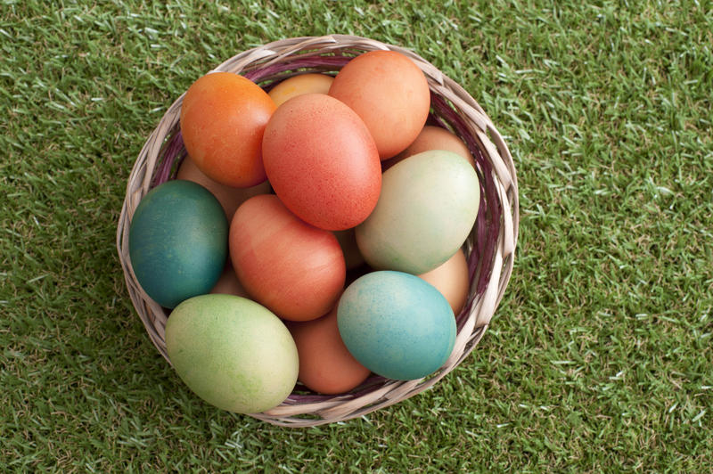 Rustic wicker basket filled with traditional homemade dyed easter eggs in lovely pastel colors on green spring grass viewed from above