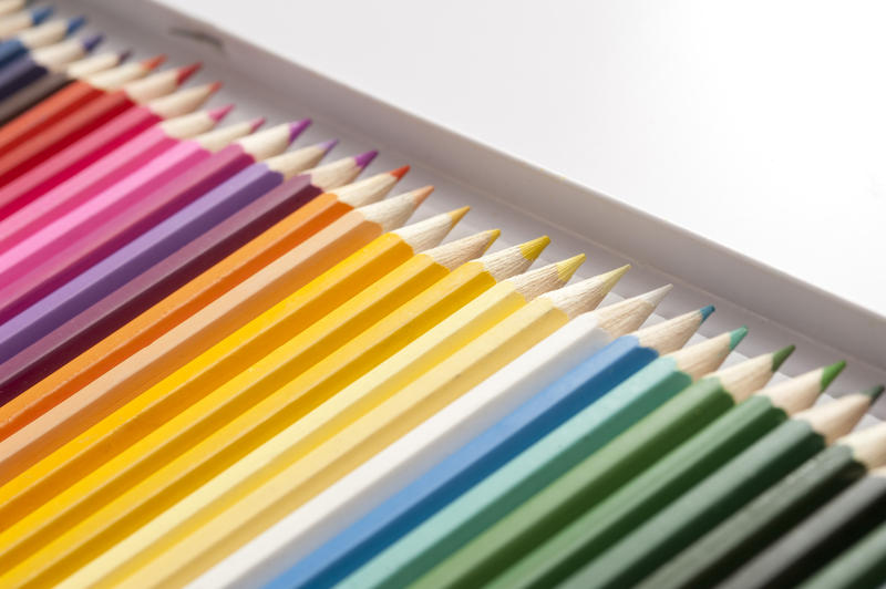 Open box of newly sharpened pencils in dark and bright colors arranged in a long row with selective focus