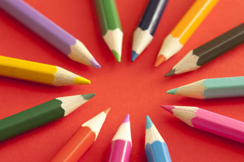 Circle pattern of sharpened colored pencils pointing toward each other over red background