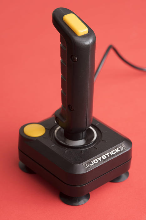 Retro old black joystick for video games over a red background in a close up view in a concept pf entertainment and technology