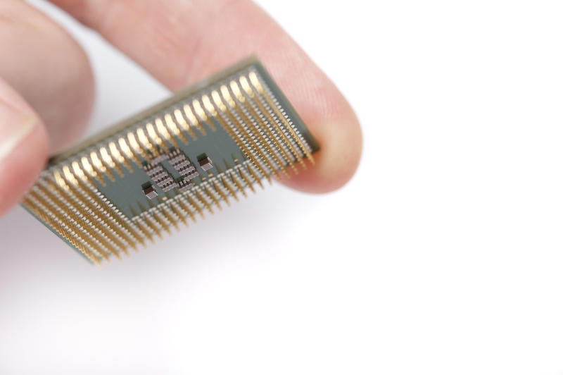 Close up macro view of a computer microprocessor held between the fingers of person over white with copy space