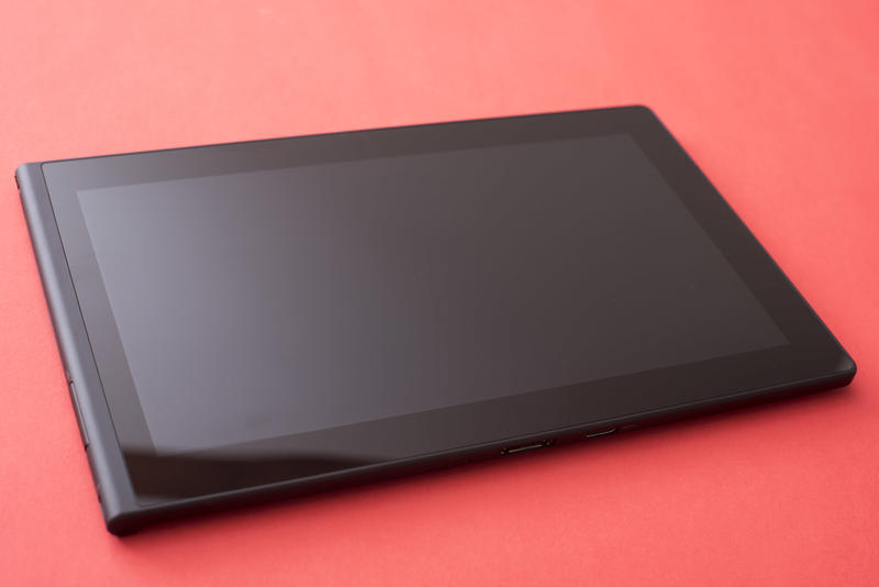 Black computer tablet with screen turned off close-up on plain red background