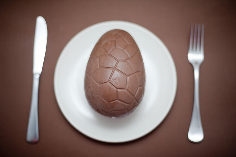 Serving of one chocolate Easter Egg for dinner on a white plate flanked by a knife and fork over a brown background in a fun concept