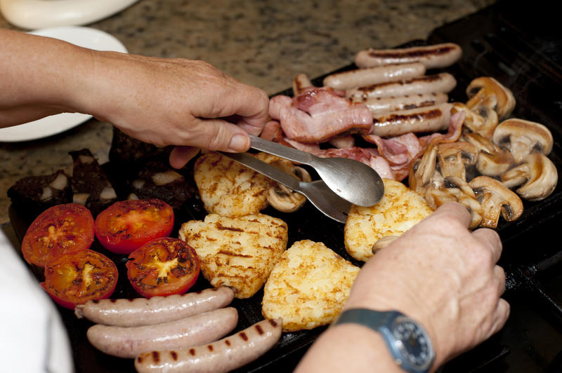 Chef uses tongs to flip food pieces being cooked on kitchen stove top while wearing watch