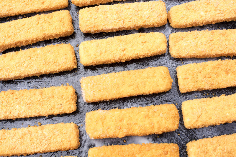 Breaded fish fingers laid out neatly in rows on an baking tray conceptual of convenience and fast food snacks