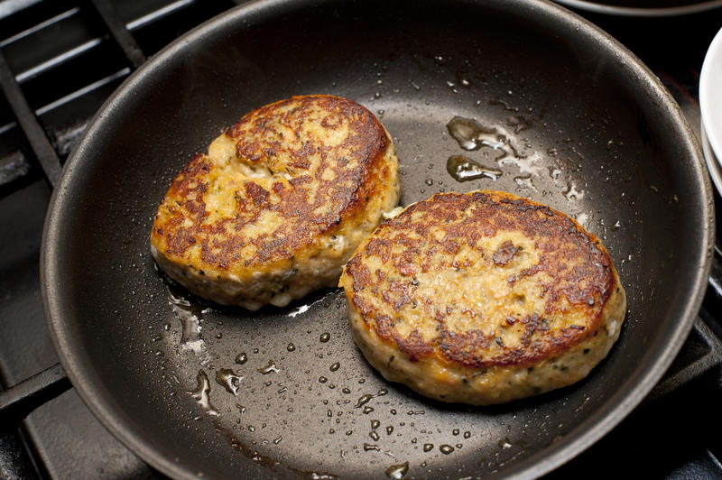 Pair of delicious fried crab-cakes in non-stick frying pan with melted butter globules
