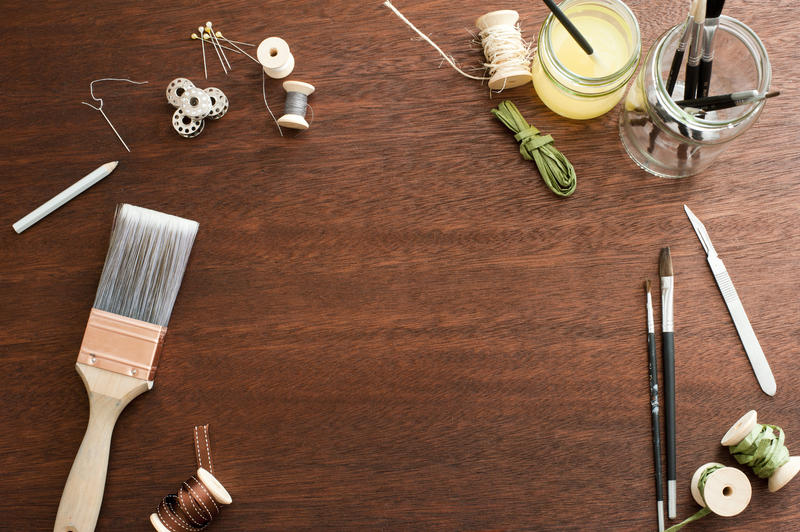 Random paint brushes, spools, knife and jars as frame around copy space on wooden table background