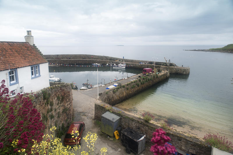 Wide angle view from hillside of Fife Coast harbor under partly cloudy sky in Crail, Scotland