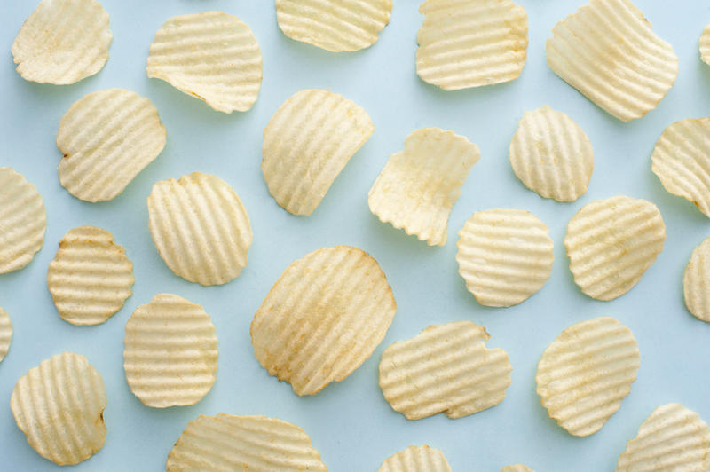 Full background of salty crispy yellow ridged oval shaped potato chips over blue surface