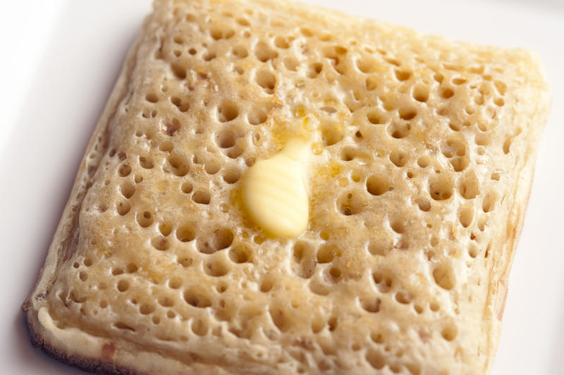 Close up on holes in top of delicious square shaped crumpet and melting butter on top