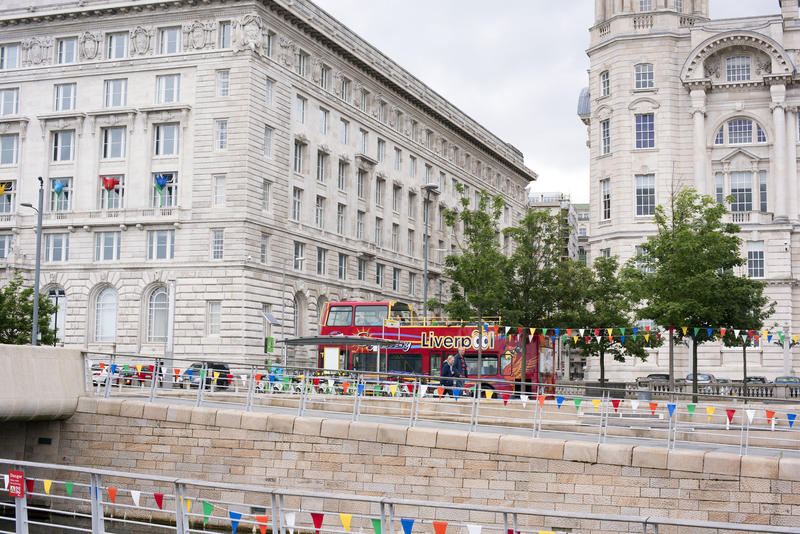 Single red tourist bus parked near in front of one of the three graces, Liverpool, United Kingdom