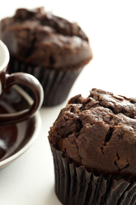 Dark brown freshly baked chocolate muffin served with a cup of tea of coffee, close up partial views of the cookie and cup
