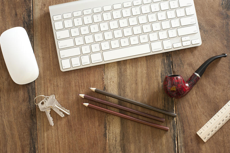 a modern wooden desk with wireless keyboard, pencils and a smokers pipe