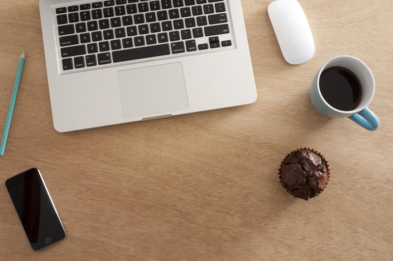 Office desk still life viewed from above with an open laptop computer, muffin, mobile phone, mouse and cup of hot coffee