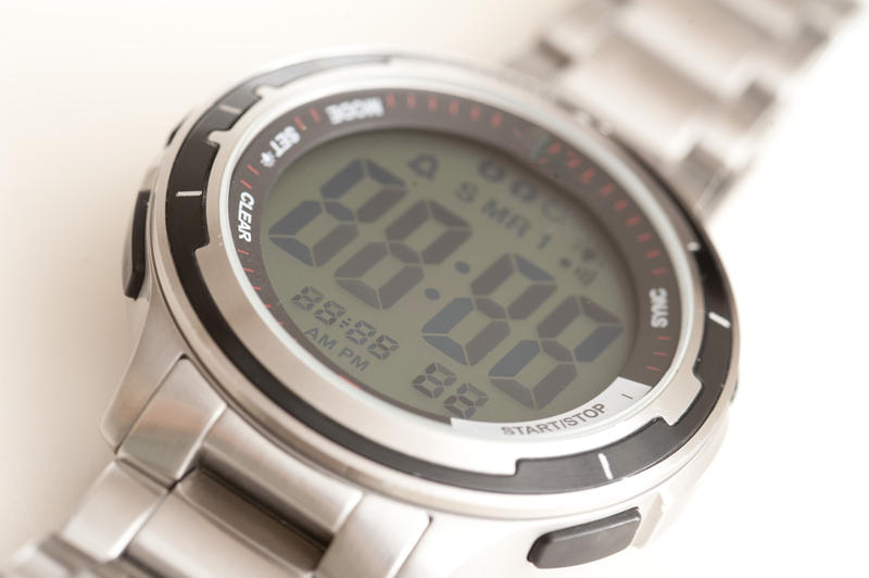 Digital wrist watch with a shiny silver metal case and large LCD numbers on the face, close up on white
