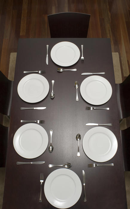 Dark wood dining table laid with clean empty white plates and cutlery for six but no food viewed from above