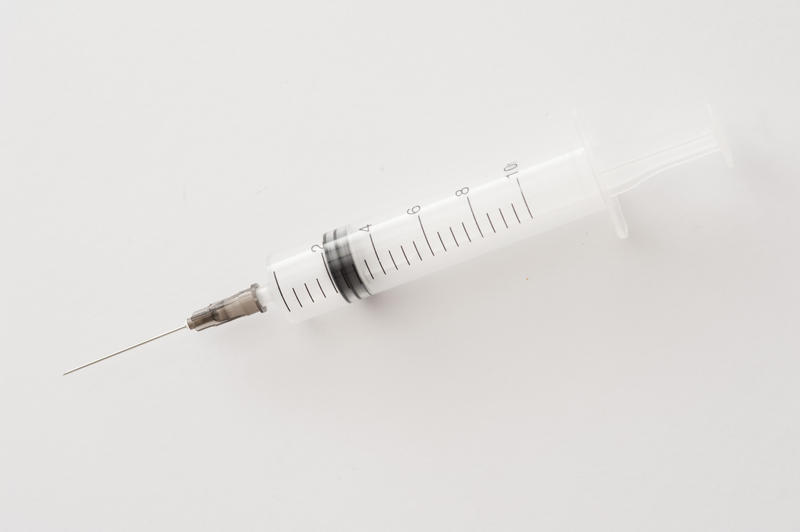 Single large empty clear plastic syringe with long needle over white background. Includes copy space.