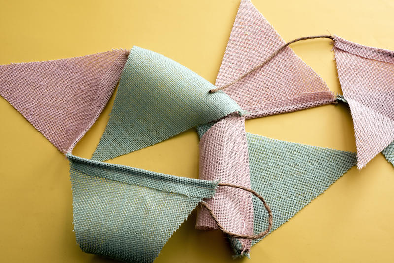 Close-up view of fabric triangle flag garland laying on yellow surface background. Easter bunting concept
