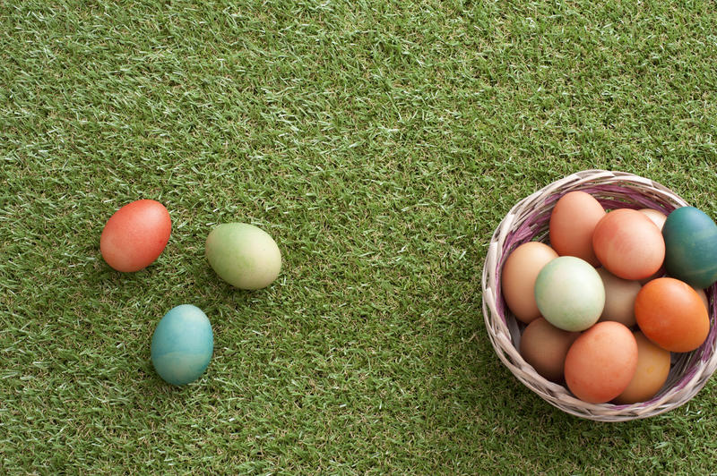 Wicker bowl basket full of dyed Easter eggs with some colored eggs over green loan grass. Easter concept with copy space