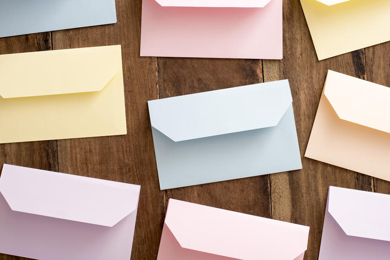 Still life of colored Easter envelopes lying face down with open flaps on a wooden background viewed from overhead