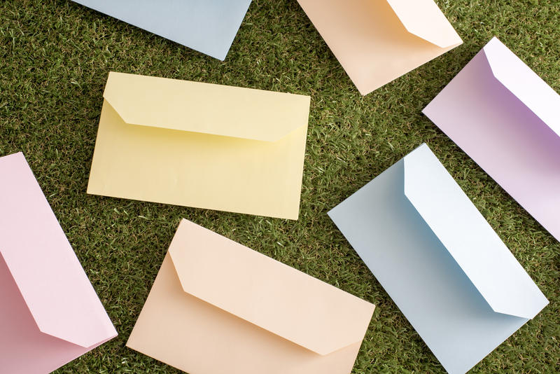 Colorful scattered envelopes for Easter greetings lying flap side up on green grass in a full frame background