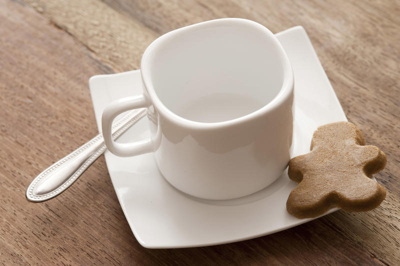 Clean white coffee cup and saucer with a silver teaspoon and gingerbread man cookie on a wooden table