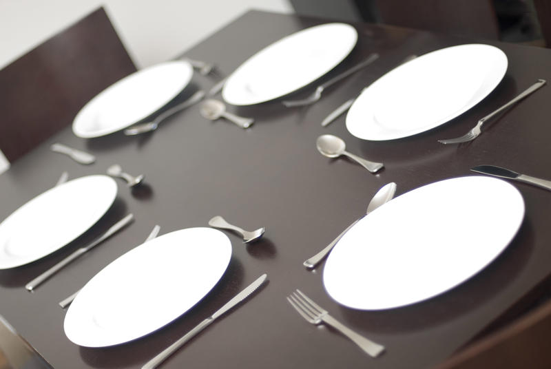 Empty clean white dinner plates on a table with cutlery set for six people in a tilted view