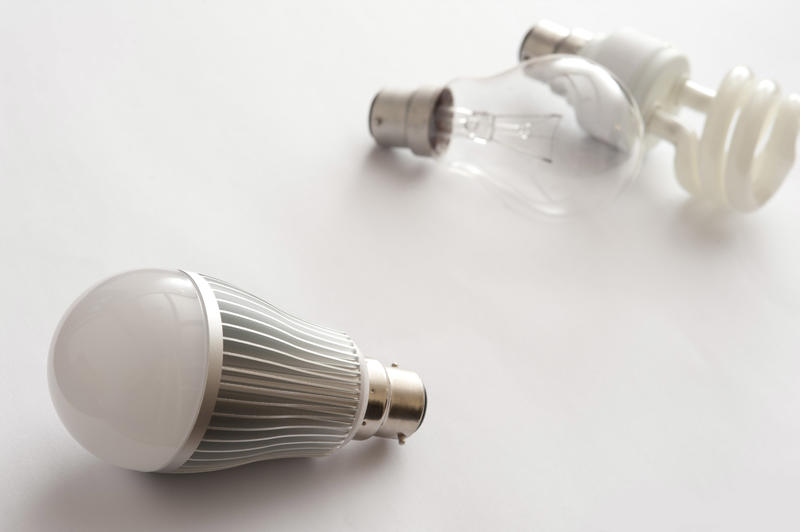 Three generations of light bulbs, with LED energy efficient lamp close-up in focus and incandescent with fluorescent lamps blurred in background on white surface