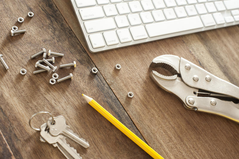 Engineering background concept with nuts, bolts, a mole grip, pencil, keys and computer keyboard on a wooden background, high angle view