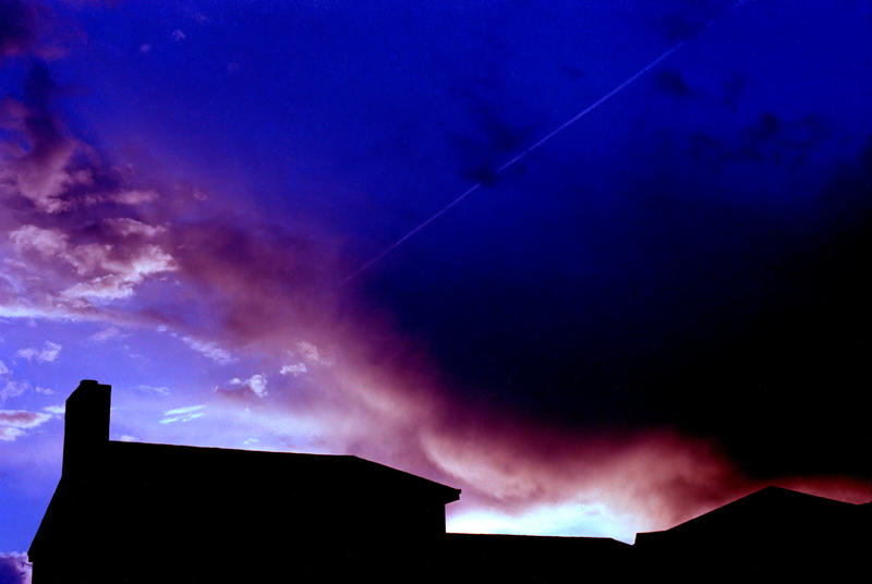 <p>Evening storm clouds can be seen forming over residential housing in this vintage film scan. A jet entrail is visible within the clouds.</p>