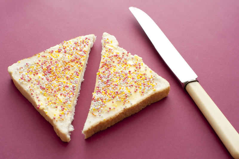 Serving of fairybread covered in red, yellow and white sugary candy drops cut in half with knife