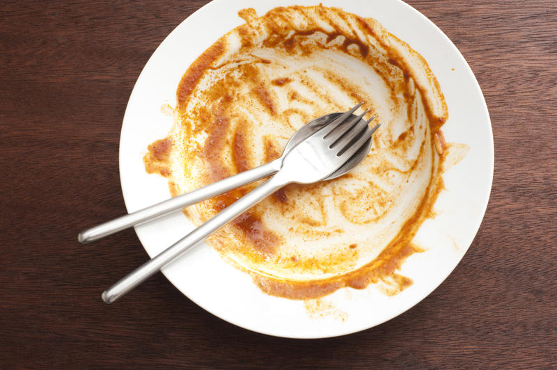 Dirty plate after a finished meal scraped clean with a silver spoon and fork neatly arranged to the centre viewed from above