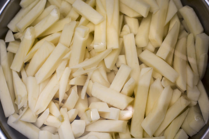 Freshly prepared raw potato chips in a container ready for cooking, close up overhead view