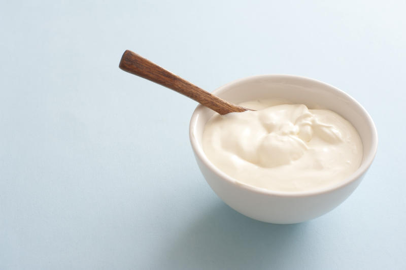 Bowl of fresh sour cream with spoon and copy space over a light grey background to be served as an accompaniment or topping