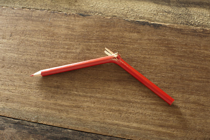 Frustrated concept with a red pencil crayon snapped in half and left lying on a wooden table in a fit of anger