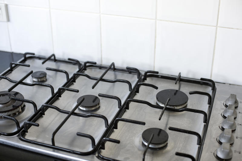 Gas stove with five unlit burner plates on the hob in a white tiled kitchen