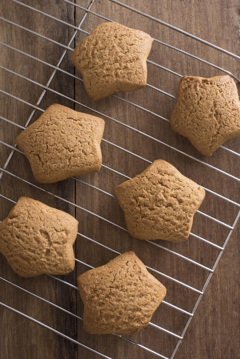 Freshly baked gingerbread star cookies cooling on a metal rack on a wooden kitchen table ready for Christmas celebrations