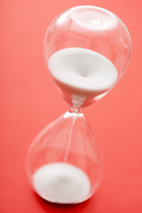 Grains of white sand in an hourglass or egg timer running through the glass bulbs measuring the passage of time over a red background