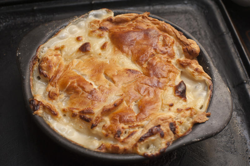 Gratinated or au gratin pie topping with breadcrumbs, butter and melted cheese in a cast iron casserole dish on a kitchen table