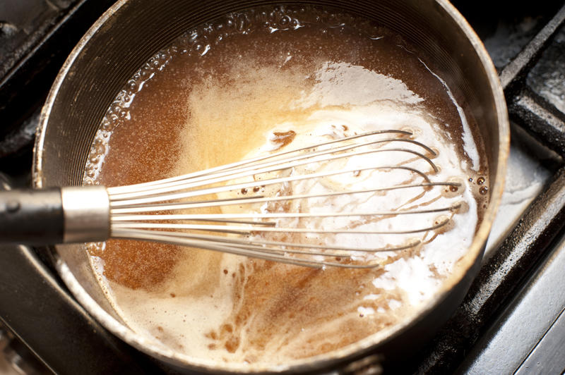 Whisking rich gravy from meat juices in a pot over a hotplate with a manual metal whisk to prevent lumps forming