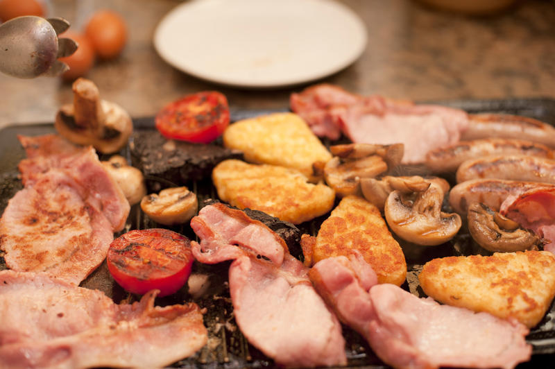 Wholesome English breakfast cooking on the griddle with bacon, hash browns, sausages, tomatoes and mushrooms